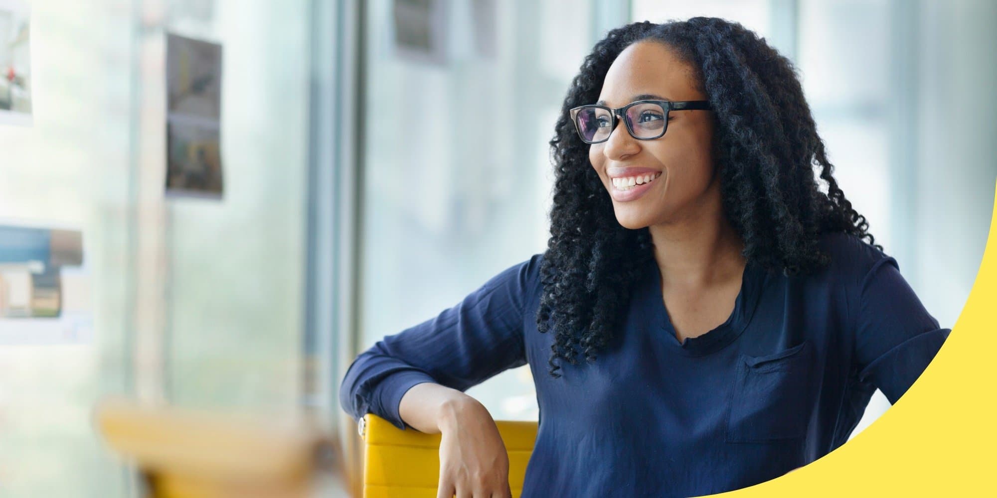 person looking off to the side and smiling while sitting in yellow chair in front of windows